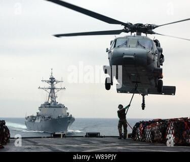 A flight deck crew member aboard the USNS Arctic (T-AOE 8) attaches a cargo pendant onto the hook of an MH-60S Seahawk helicopter during a vertical replenishment with the guided missile destroyer USS Mason (DDG 87) as the ships steam in the Persian Gulf on Feb. 25, 2005.  The Artic is a Military Sealift Command fast combat support ship. Stock Photo