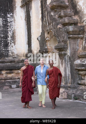 A Female Tourist and Two Burmese Buddhist Monks Walking Together and Smiling at the Camera in an Ancient Temple in Bagan Myanmar-Tourist is Released. Stock Photo
