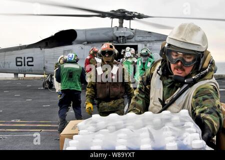 U.S. sailors and Marines aboard the aircraft carrier USS Ronald Reagan load humanitarian assistance supplies onto an HH-60H Seahawk helicopter assigned to Anti-Submarine Squadron 4 in the Pacific Ocean on March 19, 2011.  The Ronald Reagan is operating off the coast of Japan providing humanitarian assistance to support Operation Tomodachi. Stock Photo