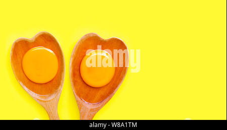 Egg yolk and white on  wooden spoon heart shape on yellow background. Top view Stock Photo