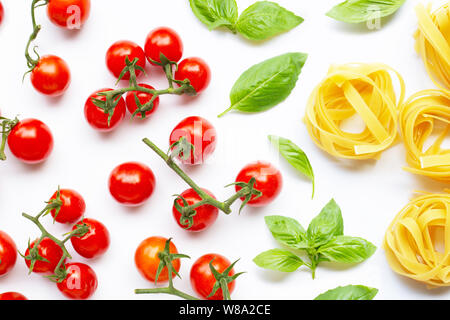 Cherry tomatoes with  basil leaves  and uncooked pasta tagliatelle nest on white background. Italian food concept Stock Photo