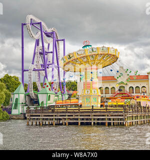Merry go round carousel ride and roller coaster at Tivoli Grona Lund amusement park Stockholm Sweden seen from Lake Malaren gray storm clouds threaten