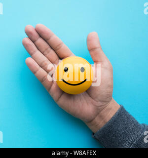 Mele hand holding yellow  emoticon ball on blue color background Stock Photo