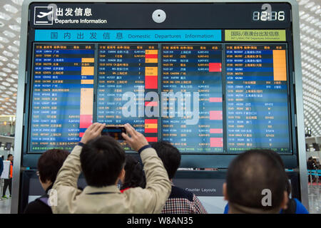 --FILE--Passengers look at an electronic display showing that most flights were delayed or cancelled due to bad weather at the Shenzhen Baoan Internat Stock Photo