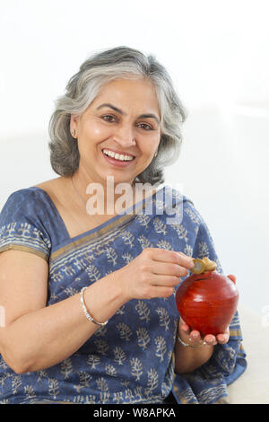 Senior woman saving money putting a coin inside piggy bank pointing and ...