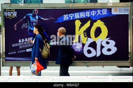 --FILE--Pedestrians walk past an advertisement for Suning.com, the online shopping site of home appliances chain Suning, at a bus stop in Yichang city Stock Photo
