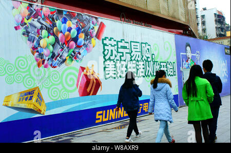 --FILE--Pedestrians walk past an advertisement for Suning.com, the online shopping site of home appliances chain Suning, in Yichang city, central Chin Stock Photo