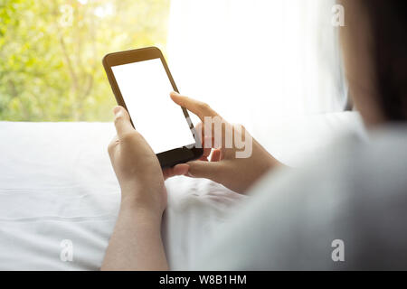 Woman using (holding) smartphone on bed in morning with window view.lifestyle activity concepts ideas Stock Photo