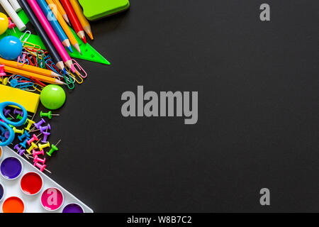 Top view on blackboard with school supplies. Multi colored vibrant pencils, paints, paper clips and other objects. Copy space. Stock Photo