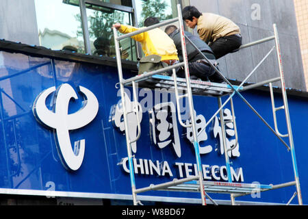 --FILE--Chinese workers install a signage at a branch of China Telecom in Yunyang county, Chongqing, 23 March 2016.   China Unicom and China Telecom s Stock Photo