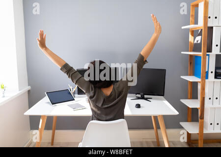 Rear View Of Young Businesswoman Stretching Her Arms In Office Stock Photo