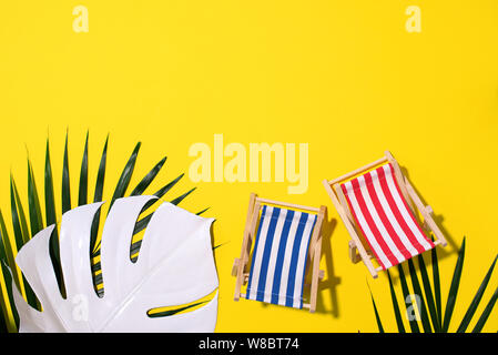 Two deck chairs with hard shadow, monstera and palm leaves on yellow paper background. Flat lay and copy space. Summer travel vacation concept. Minimal composition. Stock Photo