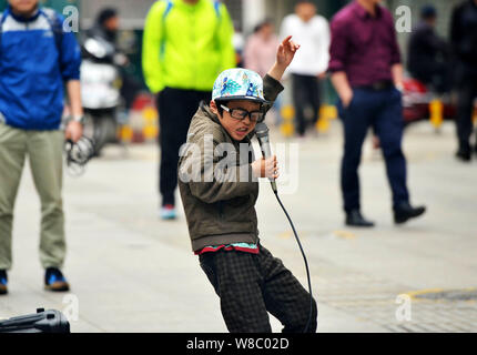 Nine-year-old boy Ye Jianjun sings a song to beg for money on a street in Changsha city, central China's Hunan province, 6 April 2016.   A young Chine Stock Photo