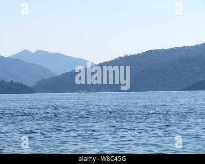 View from the sea to the mountainous islands, coast in the morning. Picturesque seascape, coastline with mountains and hills covered by forest in mist Stock Photo