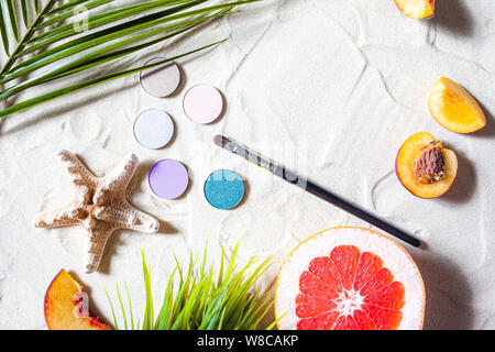 Charming beach. Round single shadows of different shades with bright fruits, a starfish, and palm leaves lie on the white sand. Close-up, top view. Stock Photo