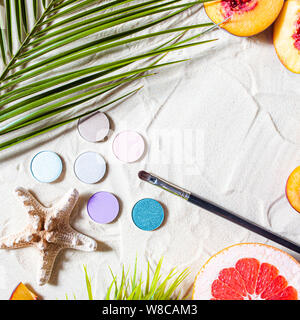 Charming beach. Round single shadows of different shades with bright fruits, a starfish, and palm leaves lie on the white sand. Close-up, top view. Stock Photo