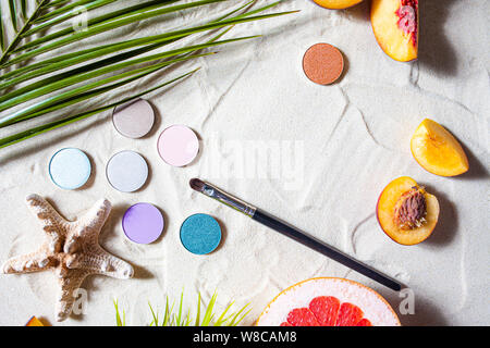 Charming beach. Round single shadows of different shades with bright fruits, a starfish, and palm leaves lie on the white sand. Close-up, top view. Stock Photo