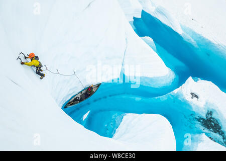 Young man ice climbing on lead heading up from a canoe on the water of a Matanuska Glacier lake in Alaska. Stock Photo