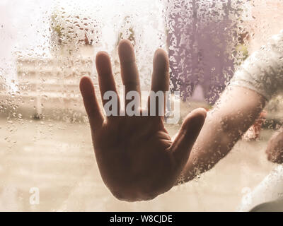 Human Hand pressed against a window with Drops Of Rain on it. Hand touching clear glass with water droplet. Natural Pattern of raindrops isolated from Stock Photo