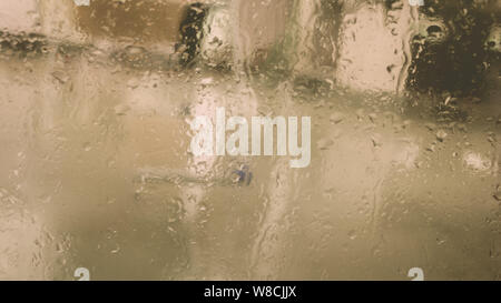 Rain Drops On Surface of wet Window Glass pane In Rainy Season. Abstract background. Natural Pattern of raindrops isolated from blurry city outdoor in Stock Photo