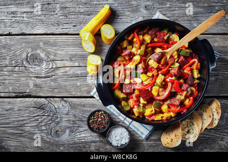 overhead view of Pisto manchego - vegetable stew with chorizo sausages in a black pan on a rustic wooden table, spanish cuisine, view from above, flat Stock Photo