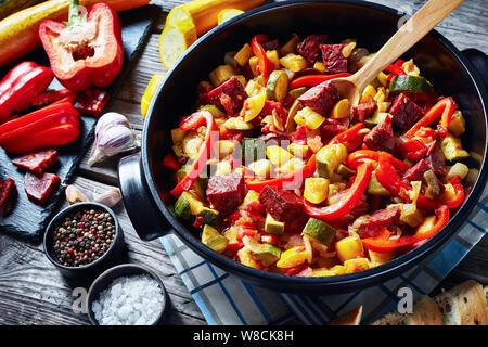 Spanish Pisto manchego - vegetable stew with fried chorizo sausages in a black pan on a rustic wooden table with ingredients, view from above, close-u Stock Photo