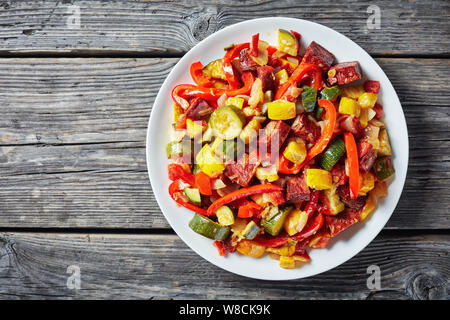 Spanish Pisto manchego - vegetable stew with fried chorizo sausages on a white plate on a rustic wooden table, view from above, empty space, flatlay Stock Photo