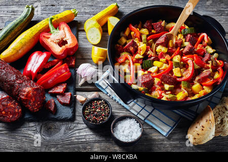 Pisto manchego - vegetable stew with chorizo sausages in a black pan on a rustic wooden table, spanish cuisine, horizontal view from above, Stock Photo