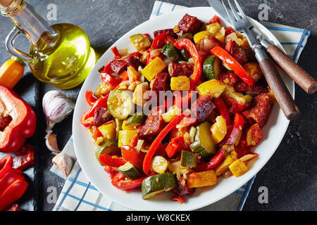 Pisto manchego - Spanish vegetable stew with fried chorizo sausages served on a white plate on a concrete table with olive oil, view from above, close Stock Photo