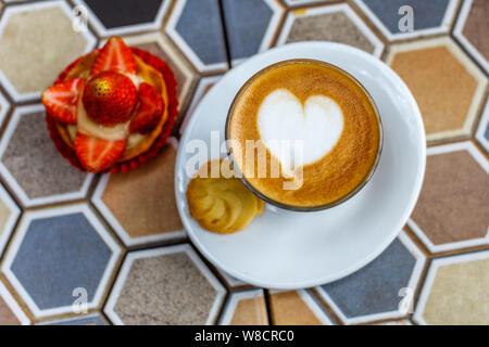 A glass of coffee latte and a strawberry tart on a colorful ceramic table in a cafe. Stock Photo