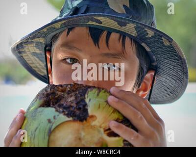 Cute little boy of mixed race (Caucasian and Southeast Asian) drinks coconut water from a fresh coconut. Stock Photo