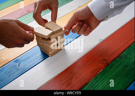 Hands of three businessmen working together to make a stack of wooden pegs in a conceptual image of business vision. Stock Photo