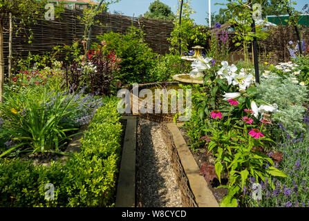 Gravel path leading to a water feature pond in a cottage flower garden in summer England UK United Kingdom GB Great Britain Stock Photo
