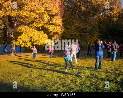 Moscow, Russia - October 11, 2018: Chinese tourists walks autumn park. Asian people take pictures on the background of a beautiful yellowed maple in Stock Photo