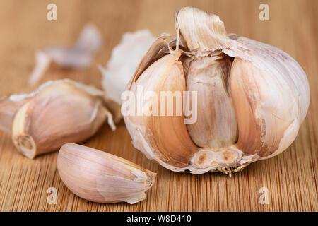 Head of garlic and several cloves of unpeeled garlic on a wooden background. Stock Photo