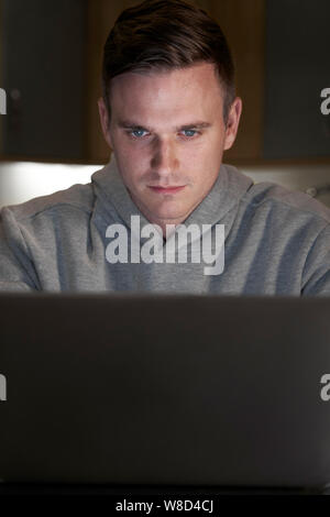 Suspicious Looking Man Using Laptop In Evening At Home Stock Photo