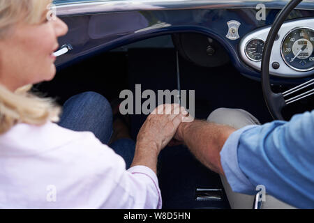 Close Up Of Loving Mature Couple Holding Hands On Road Trip In Classic Open Top Sports Car Stock Photo