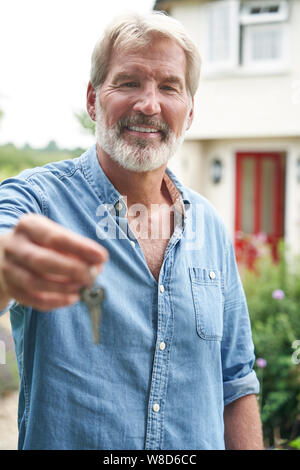 Portrait Of Mature Man Standing In Garden In Front Of Dream Home In Countryside Holding Keys Stock Photo