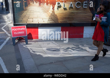 With a sign warning that the footpath (sidewalk) is closed, a pedestrian passes a construction hoarding at a new development called One Crown Place on Sun Street near Liverpool Street Station in the City of London, the capital's financial district - aka the Square Mile, on 8th August, in London, England. Stock Photo