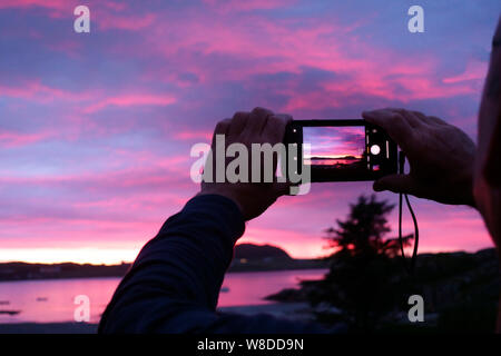 Man taking photograph of stunning sunset over Iona from Fionnphort beach, Isle of Mull, Inner Hebrides, Scotland Stock Photo