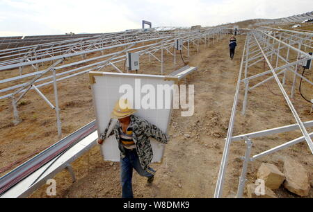Chinese workers carry solar panels to be installed at the Wanjiashan Photovoltaic Power Station on Wanjiashan Mountain in Yanbian county, Panzhihua ci Stock Photo