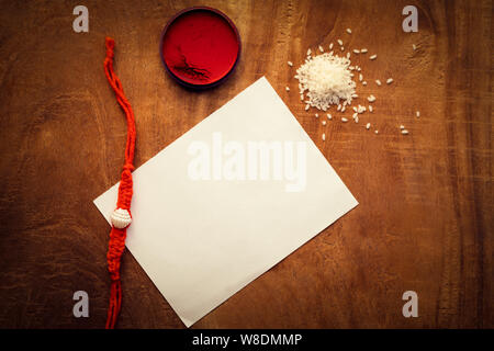 Top view of Rakhi on a wooden table with kumkum, chawal or rice grains and a white paper for copy space. Raksha Bandhan background concept. Stock Photo