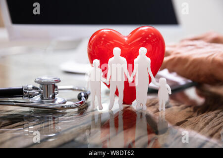 Red Heart With Family In Front Of Doctor Working On Computer Stock Photo