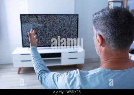 Man Sitting On Sofa In Front Of Television With No Signal Stock Photo