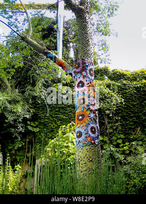 colorful crocheted fabric is wrapped around a tree bark Stock Photo