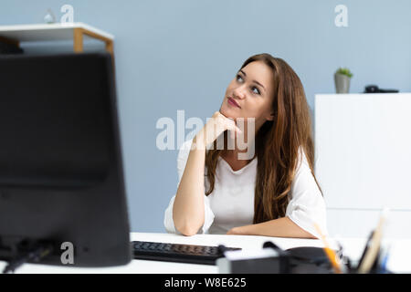 Smiling Young Businesswoman Daydreaming While Sitting In Her Office Desk Stock Photo