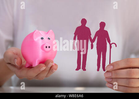 Woman's Hand Holding Pink Piggy Bank And Senior Couple Cutout Stock Photo