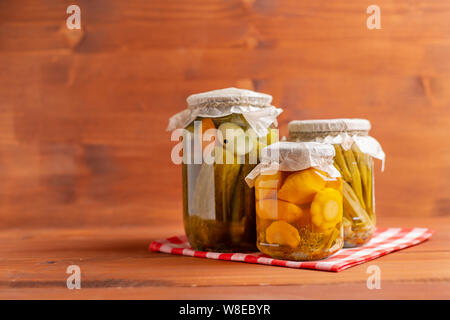 Jars of pickled vegetables: cucumbers, tomatoes, eggplants on rustic wooden background. Marinated and canned food. Stock Photo