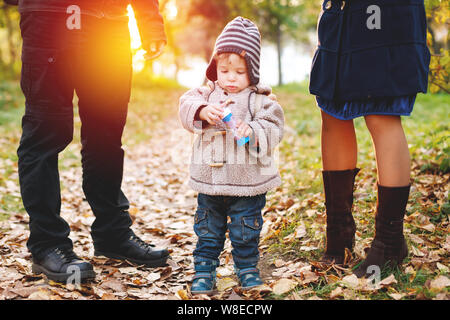 Cute two years old kid in warm clothes standing among his parents, walking un the autumn park Stock Photo