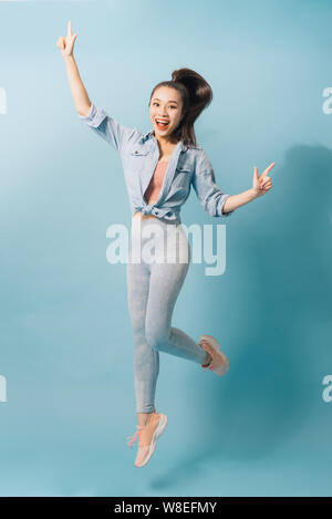 Portrait of playful crazy girl jumping in the air looking at camera enjoying weekend having perfect mood on light blue background Stock Photo